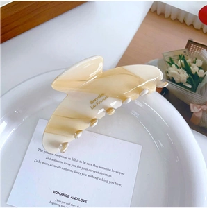 Détail d'une pince à cheveux en acétate à motif marbré avec logo doré sur assiette