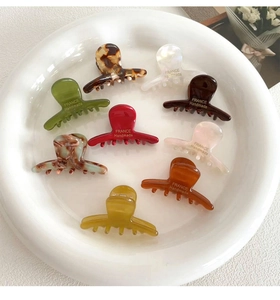 Close-up of acetate small hair claws in multiple colors arranged on a white ceramic tray