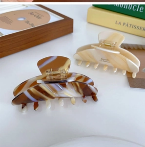 Gros plan de pinces à cheveux en acétate marbré avec détails dorés sur un bureau blanc