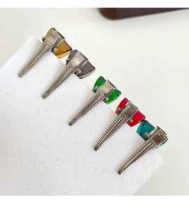 Detail of five colorful mini bow hair clips in amber, green, and red on white paper