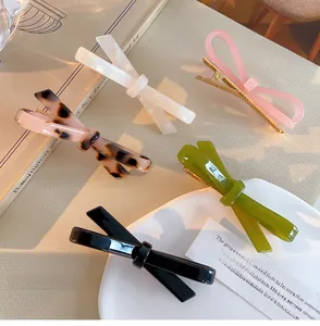 Detailed close-up of acetate bow hair clips in five colors with soft aesthetic shadows