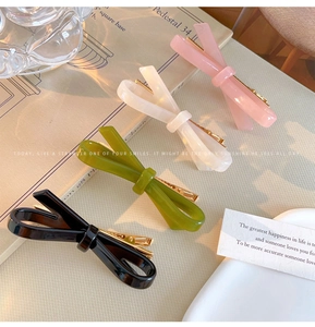 Close-up of four glossy bow-shaped acetate hair clips in pink cream green and black