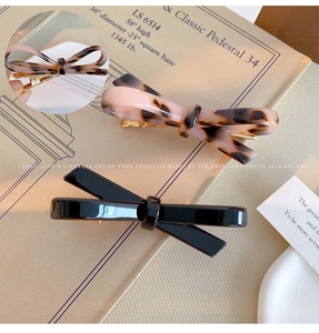 Detail view of acetate bow hair clips in pink tortoiseshell and black with gold metal grips