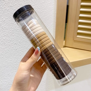 Handheld view of elastic hair ties in earth tones stored in a clear portable container