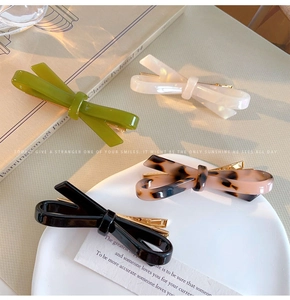 Close-up of four assorted acetate bow hair clips in green, white, and black colors