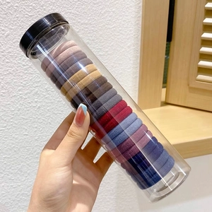 Hand holding a clear cylinder bottle filled with assorted colorful high-elastic hair ties