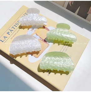 Detalle de cuatro pinzas para el cabello nacaradas en blanco y verde claro sobre un libro