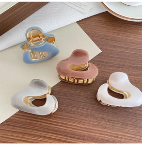 Detail of four acetate hair claws in blue, brown, grey and white with gold metal frames