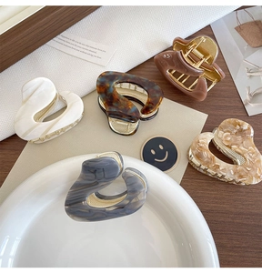 Close-up of five acetate hair claws in marble and tortoiseshell patterns with gold teeth