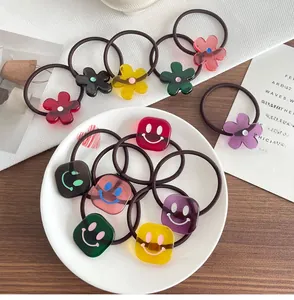 Nahaufnahme bunter Haargummis mit Smileys und Blumen aus Acryl auf weißem Teller