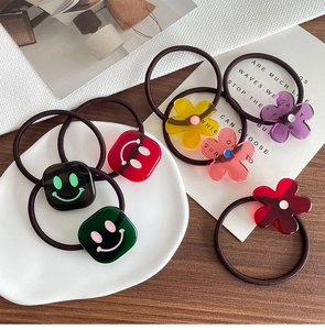 Detailansicht bunter Smiley-Quadrate und Blumenanhänger auf elastischen Haargummis