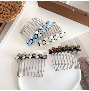 Close-up of four acetate flower hair combs in marble and pearl finishes on a white plate
