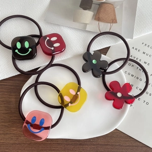 6-teiliges Set bunte Haargummis mit lachendem Gesicht und Blumen auf einem Keramikteller
