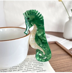 Détail d'une pince à cheveux hippocampe en acétate marbré vert sur une tasse blanche