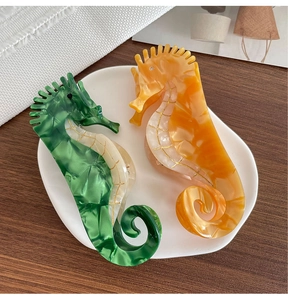 Détail de pinces à cheveux hippocampe en acétate marbré vert et orange sur plateau blanc