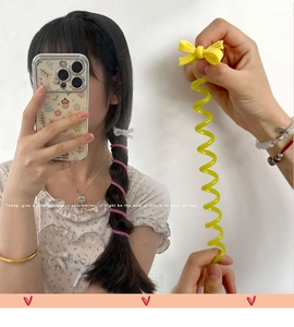 Close-up of flexible yellow spiral phone cord hair tie with a decorative acetate bow