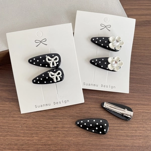 Black polka dot duckbill hair clips with white bows and floral accents on wood background