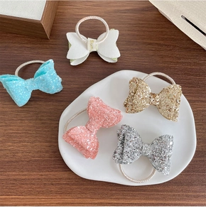 Détail de cinq élastiques à cheveux nœuds à paillettes colorés sur table en bois et plateau