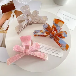 Detailed view of three marble pattern acetate bow hair claws in pink, blue, and grey