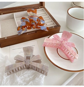 Three acetate hair claws with bow design in marble patterns on wooden jewelry box