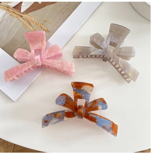 Three acetate hair claws with bow shapes and marble patterns on white surface