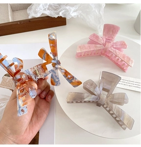 Detail of three acetate bow hair claws in pink, tortoiseshell, and marble grey colors
