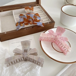 Three elegant acetate bow hair claws in blue, pink, and grey marble patterns on a wooden tray