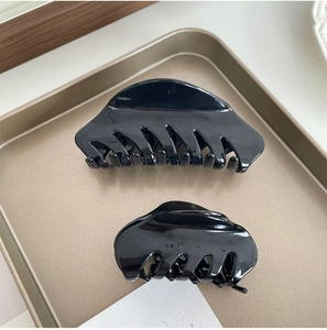 Macro detail of glossy black acetate hair claw set displayed on a champagne gold metal tray