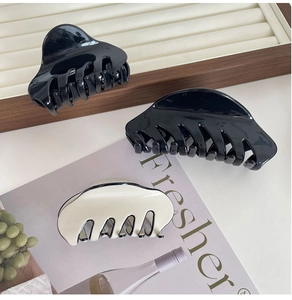 Classic large acetate hair claws in black and cream beige on a wooden jewelry tray