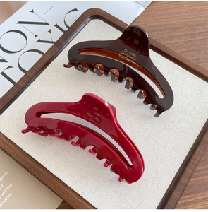Detail view of French acetate hair claws in dark brown and red with gold branding
