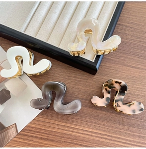 Macro shot of wave-shaped acetate hair claws in four colors with gold metal base