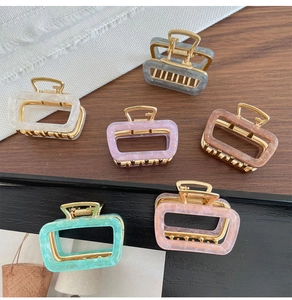 Set of six colorful rectangular acetate hair claws with metallic gold base on wood