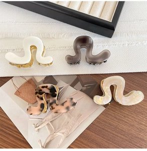 Close-up of four wavy acetate hair claws in white, leopard print, and gray marble finishes
