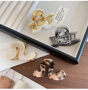 Close-up of four acetic acid hair clips in cream, pearl, and tortoiseshell on a wooden tray