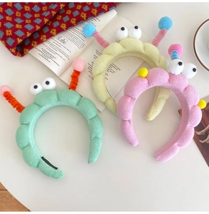 Three plush cartoon headbands in mint, pink, and yellow with big eyes and antennas