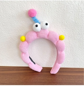 Detail of pink plush headband with large cartoon eyes and 'HAND MADE' woven label