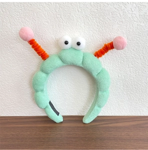 Close-up of cute cartoon plush headband with big eyes and orange spiral antennas on wood