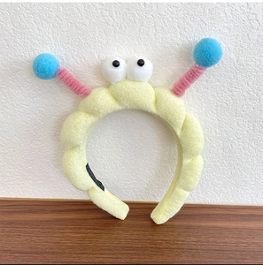 Close-up of yellow wavy plush headband with large eyes and colorful pom-poms details