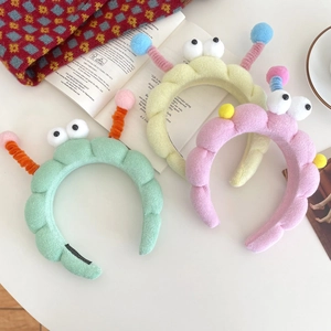 Three plush cartoon headbands with big eyes and colorful antennas in a cozy home setting
