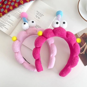 Cute cartoon plush headbands with big eyes and pom-poms on a white desk with a book