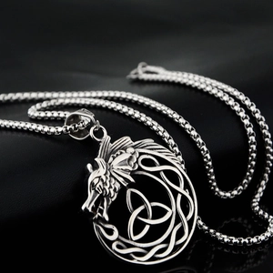Close-up of dragon head celtic knot pendant on steel chain over black leather background