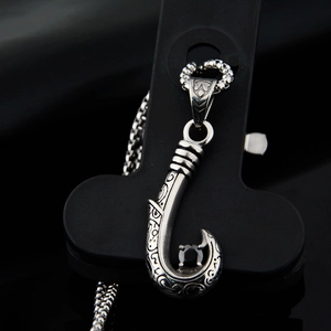Close-up of vintage steel fish hook pendant with tribal carvings and black zircon stone