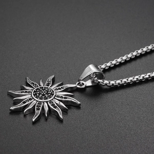 Détail d'un collier pendentif soleil en argent avec pierres noires sur fond gris mat