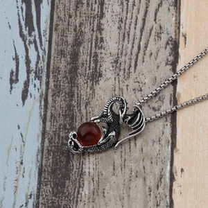 Détail d'un pendentif dragon argenté avec écailles et une perle de pierre rouge