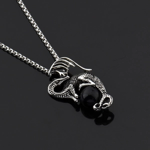 Détail macro du pendentif dragon avec perle noire et chaîne en acier inoxydable poli