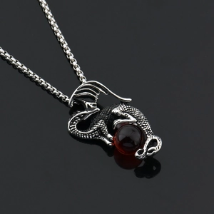 Détail d'un pendentif dragon argenté tenant une perle rouge sur chaîne gourmette