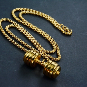 Polished gold dumbbell pendant necklace with matching box chain on dark textured background