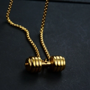 Polished gold dumbbell pendant necklace with sleek box chain on black stone background