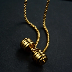 Macro shot of gold dumbbell pendant with textured grip on a steel bead chain