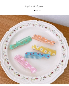Close-up of five colorful resin flower comb hair clips set in a white ceramic dish